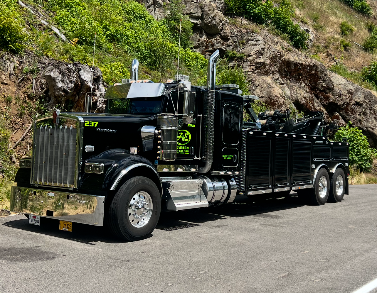 Black logging truck parked on a mountain road beside a rocky hillside.