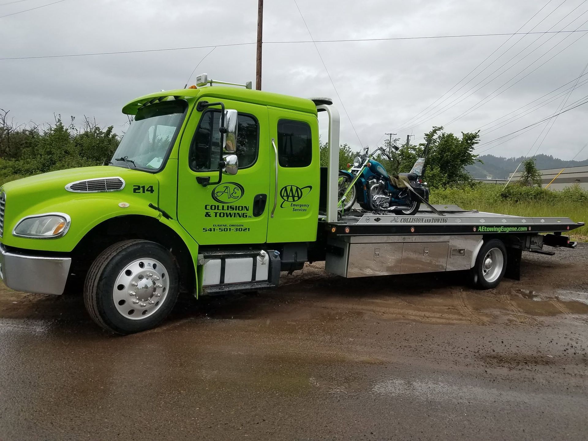 Bright green tow truck parked on a muddy roadside under cloudy skies.