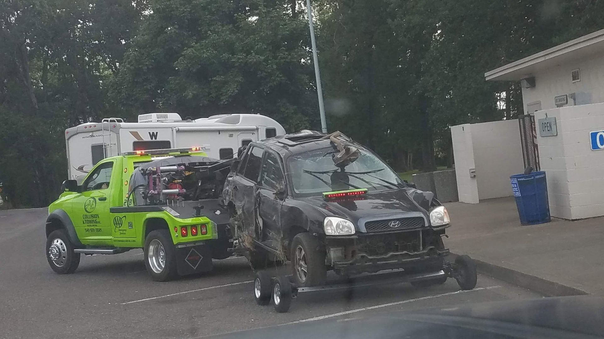 Damaged black vehicle being loaded onto a bright green tow truck in a driveway