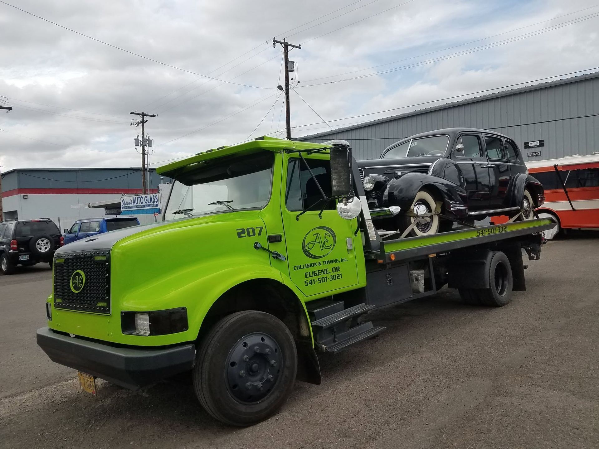 Bright green tow truck carrying a black car on a flatbed in an industrial lot