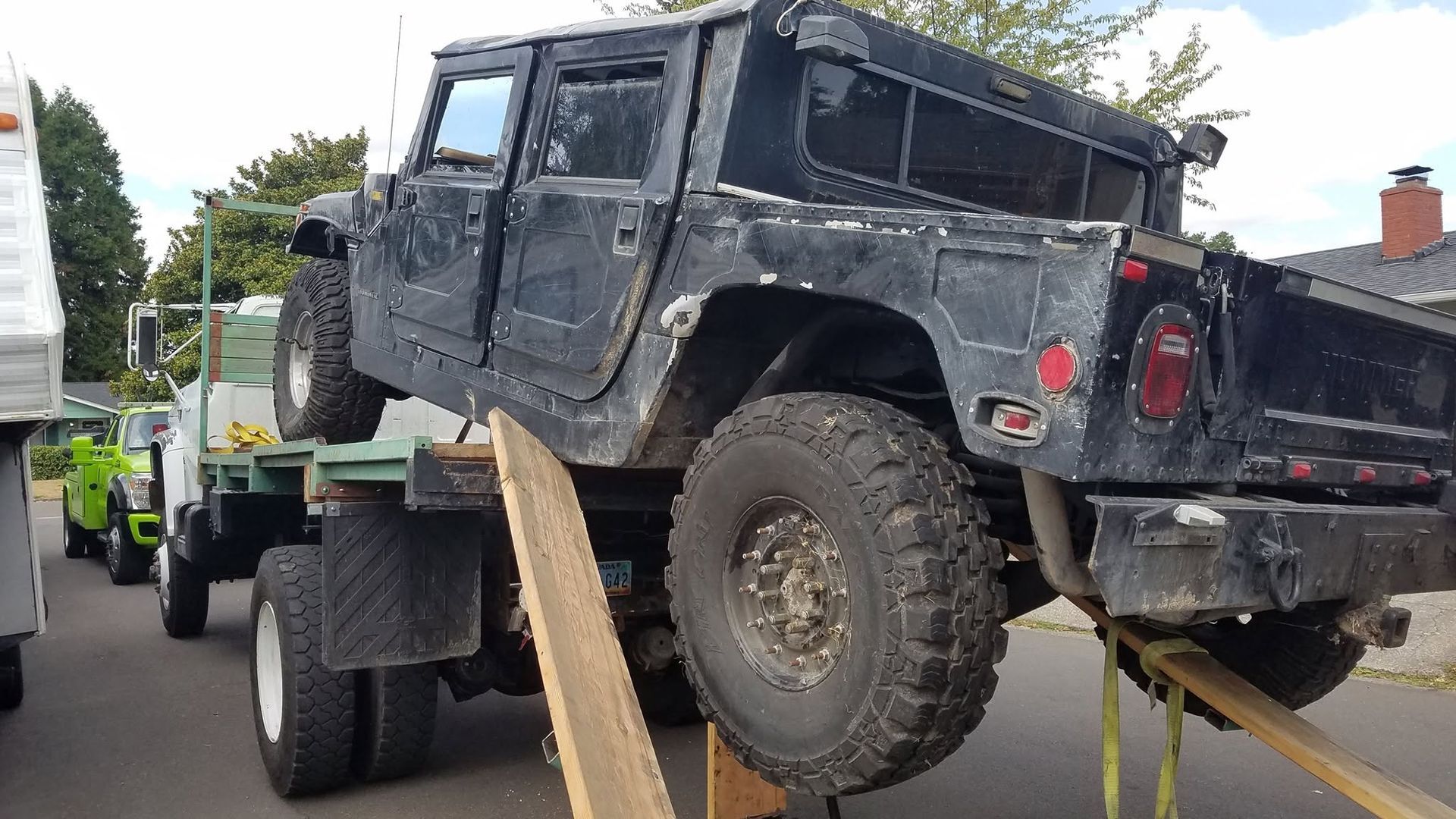 Black off-road vehicle loaded on a flatbed trailer, tilted with a ramp in a roadside setting