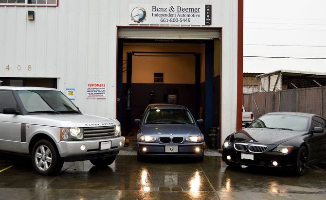 Cars outside a garage entrance on a wet day, with a black car inside and two SUVs parked at the sides