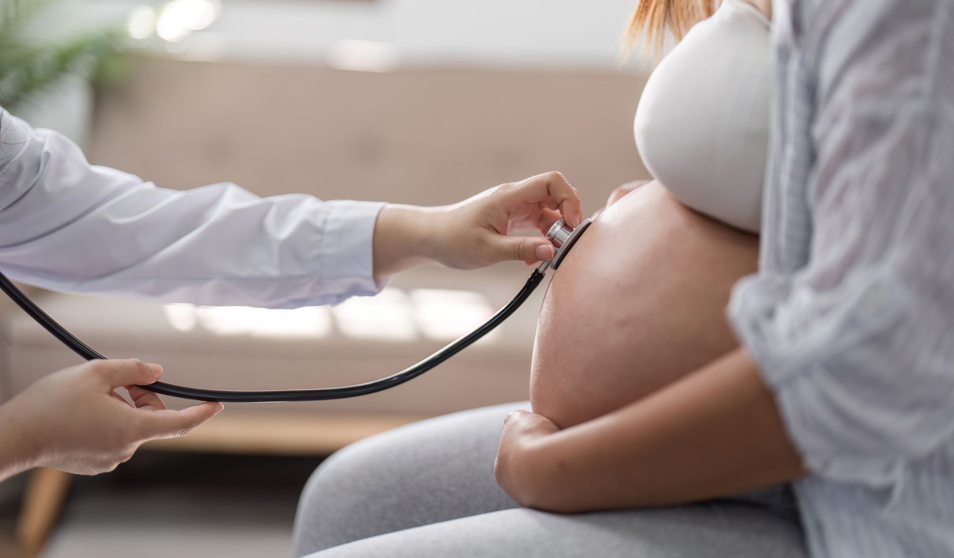 Healthcare professional using a stethoscope to check the abdomen of a pregnant patient.