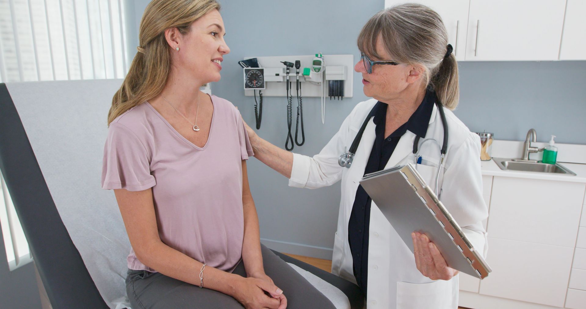 Doctor speaking with a patient during a routine exam while reviewing notes on a clipboard. Doctor speaking with a patient during a routine exam while reviewing notes on a clipboard.