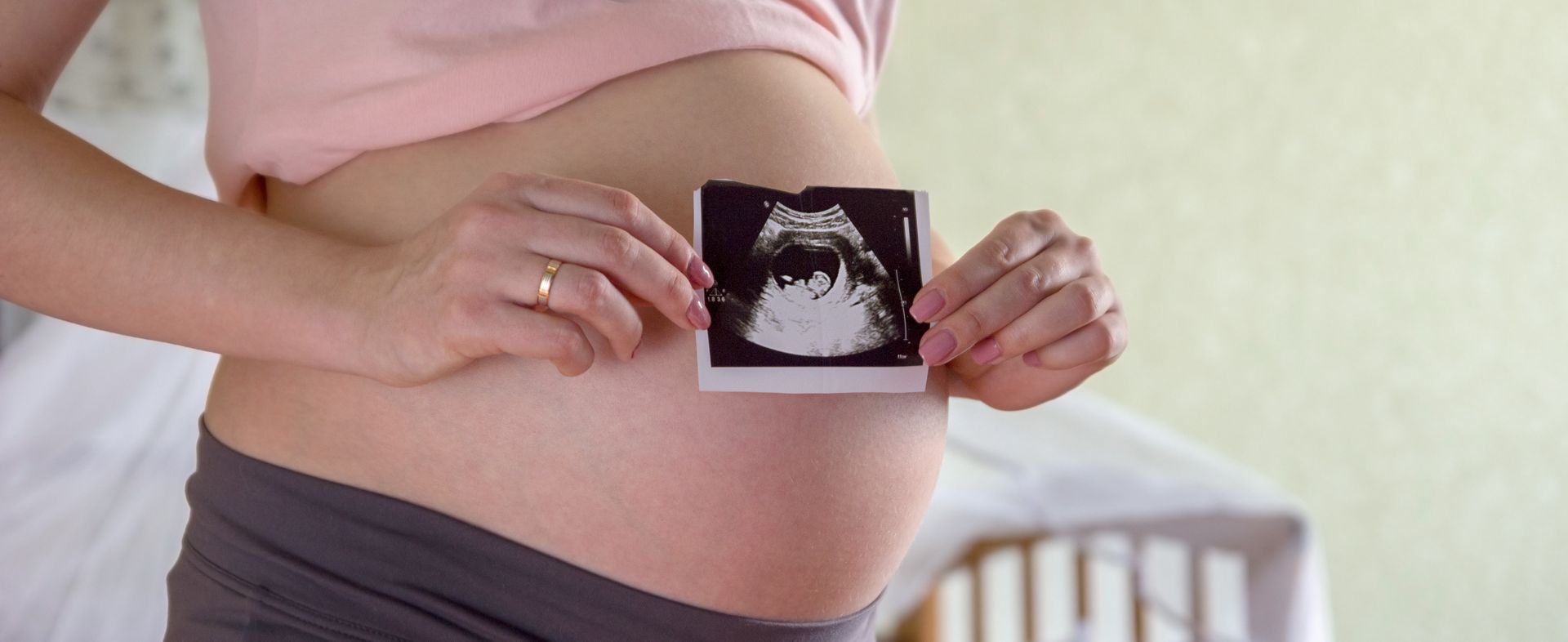 Pregnant person holding an ultrasound photo in front of a baby bump.
