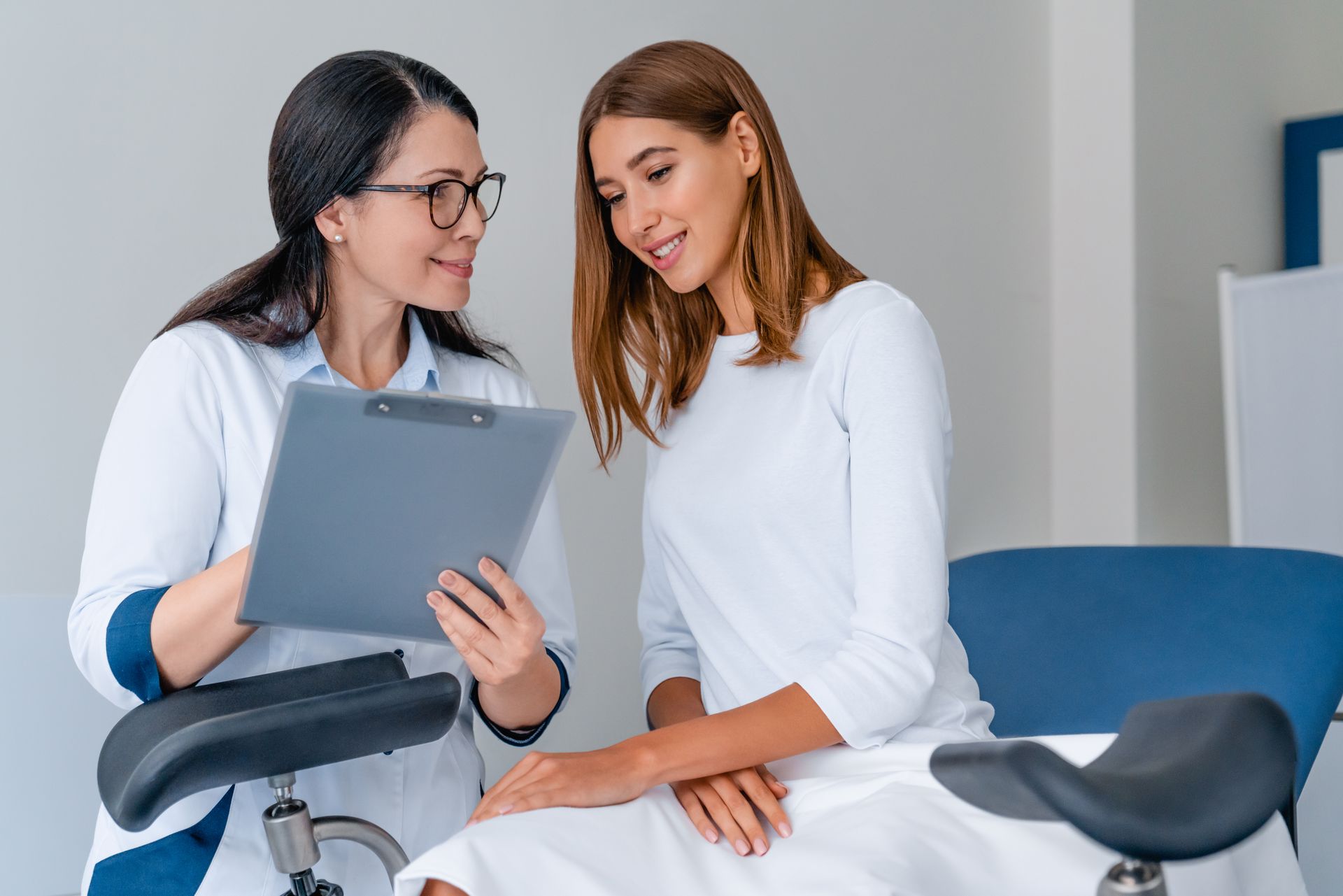 A gynecologist reviewing a clipboard with a patient during a consultation in an exam room