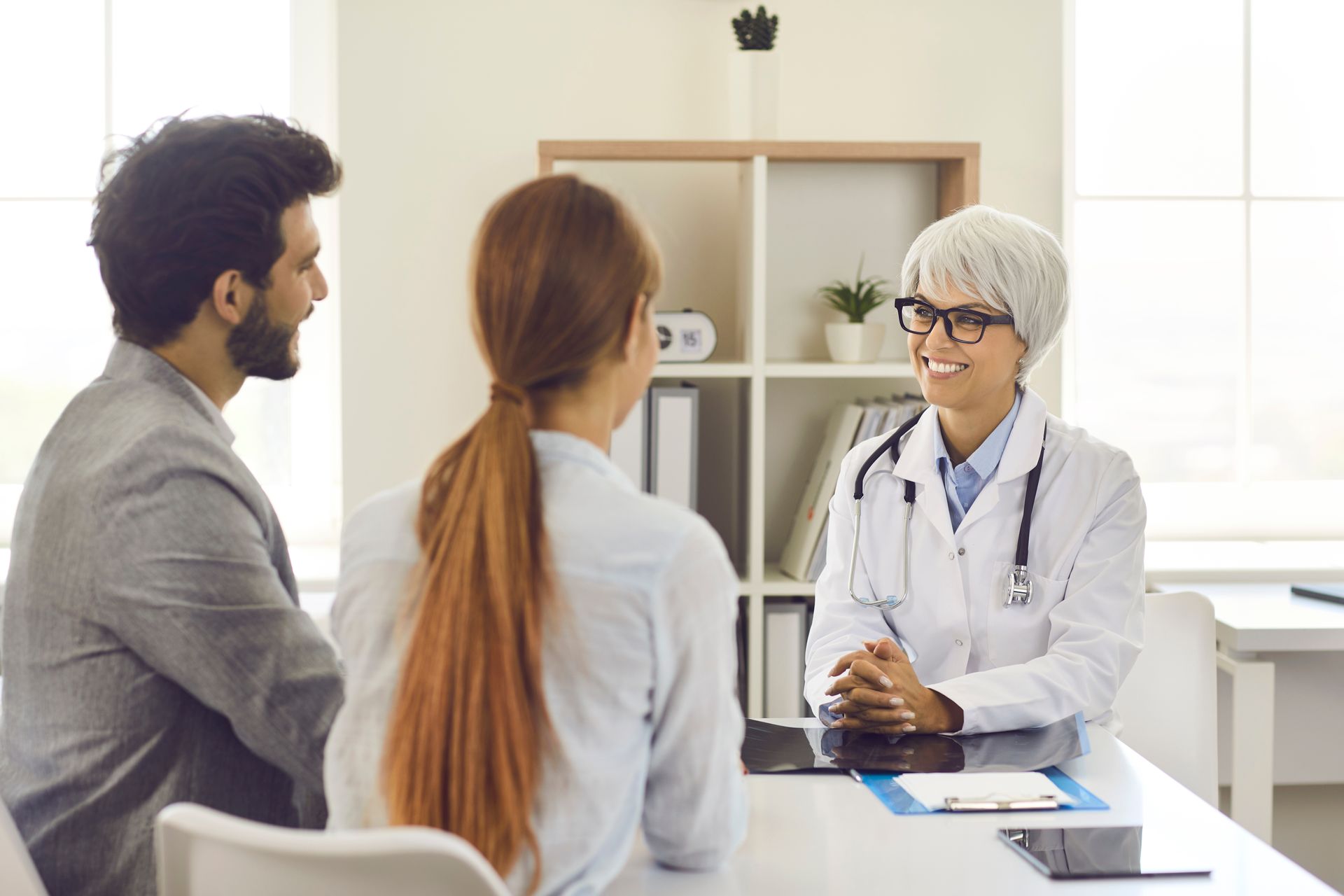 Doctor consulting with a couple in a bright office, while seated at a desk with medical tools. Doctor consulting with a couple in a bright office, while seated at a desk with medical tools.