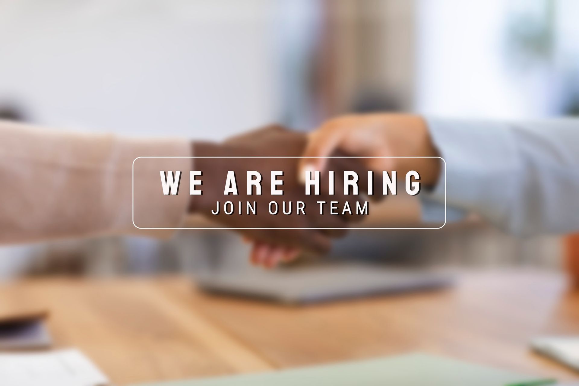 Two people shaking hands in front of a sign that says `` we are hiring join our team ''.