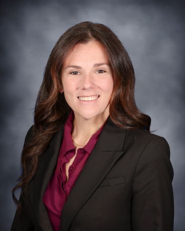 Studio portrait of a smiling woman in a black blazer and burgundy blouse on a gray background