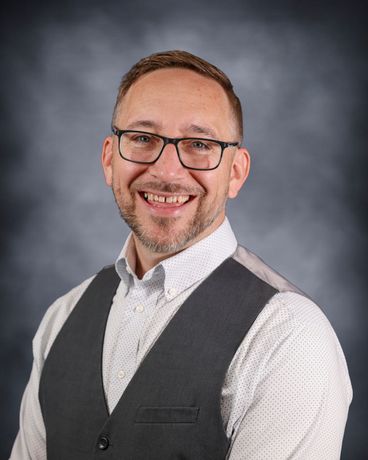 Smiling man with glasses in a patterned shirt against a gray background