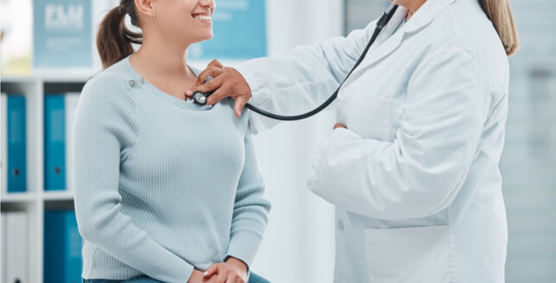 Nurse adjusts IV drip for a seated patient in a hospital room.