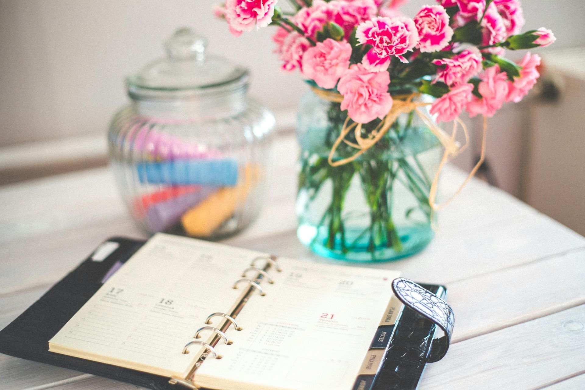 A calendar is sitting on a table next to a vase of pink flowers.