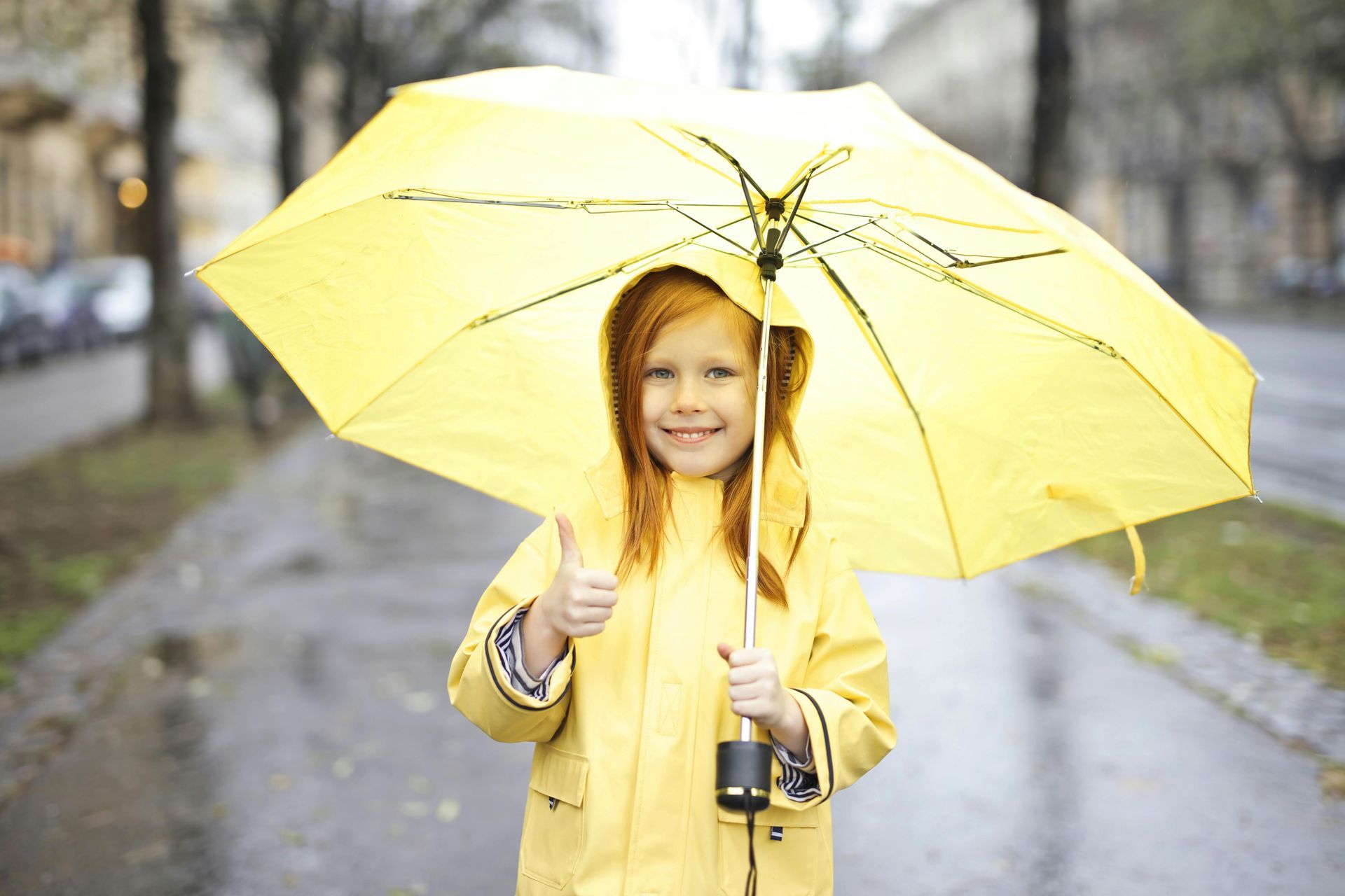 Girl dressed in a yellow raincoat under an umbrella on a rainy day
