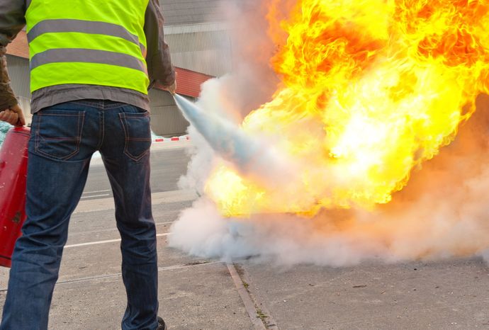 Exercice de formation à la sécurité incendie : personne en gilet jaune utilisant un extincteur pour éteindre un feu en extérieur.