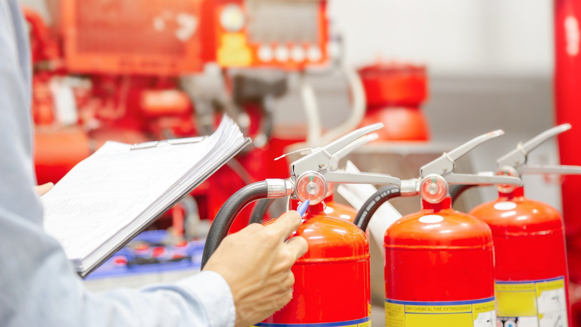 Technicien effectuant le contrôle de plusieurs extincteurs rouges avec un carnet d’inspection dans un local de sécurité incendie.