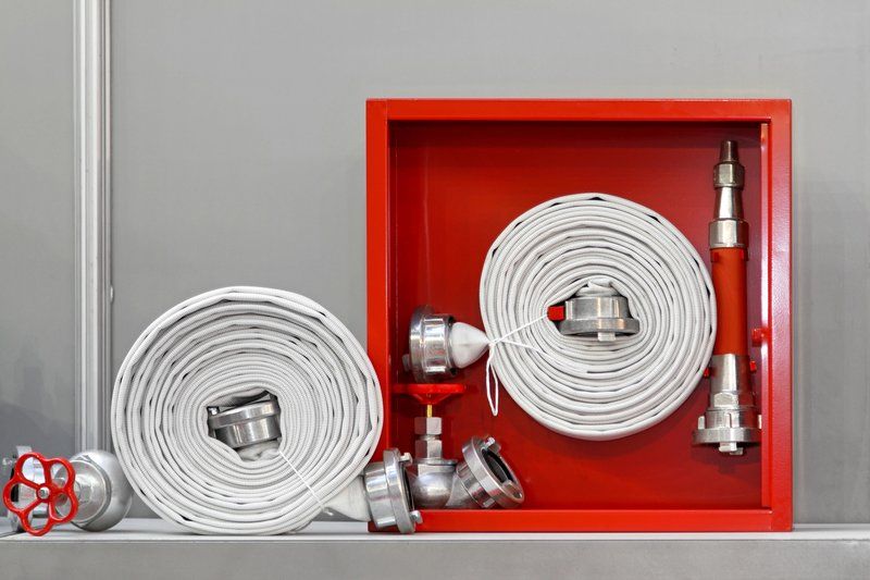 Enrouleur de tuyau souple pour robinet incendie armé (RIA), posé dans une armoire murale rouge, utilisé pour la protection incendie dans les bâtiments industriels.