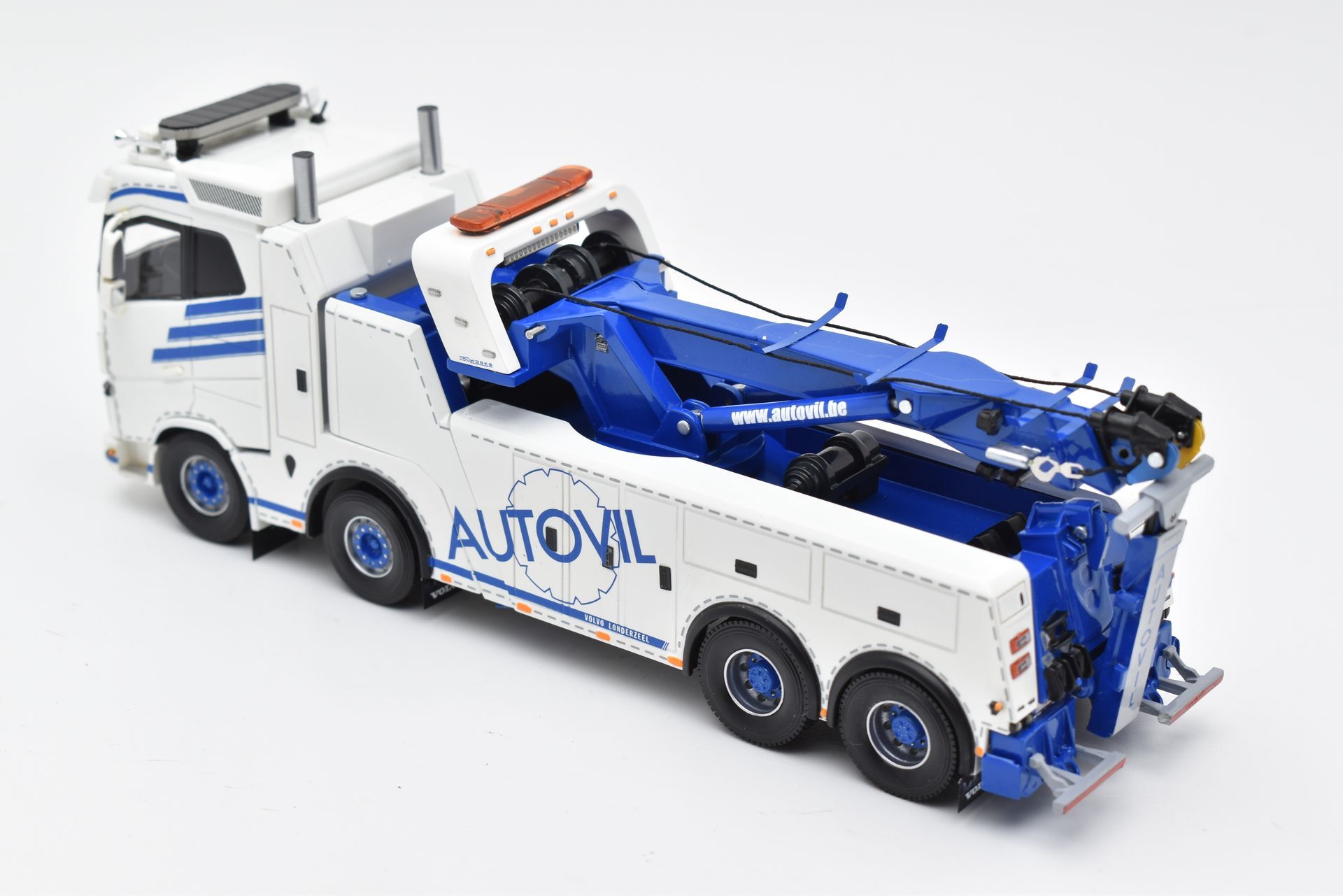 Wit-blauwe Autovil-sleepwagen met blauwe kraan op een wit oppervlak.