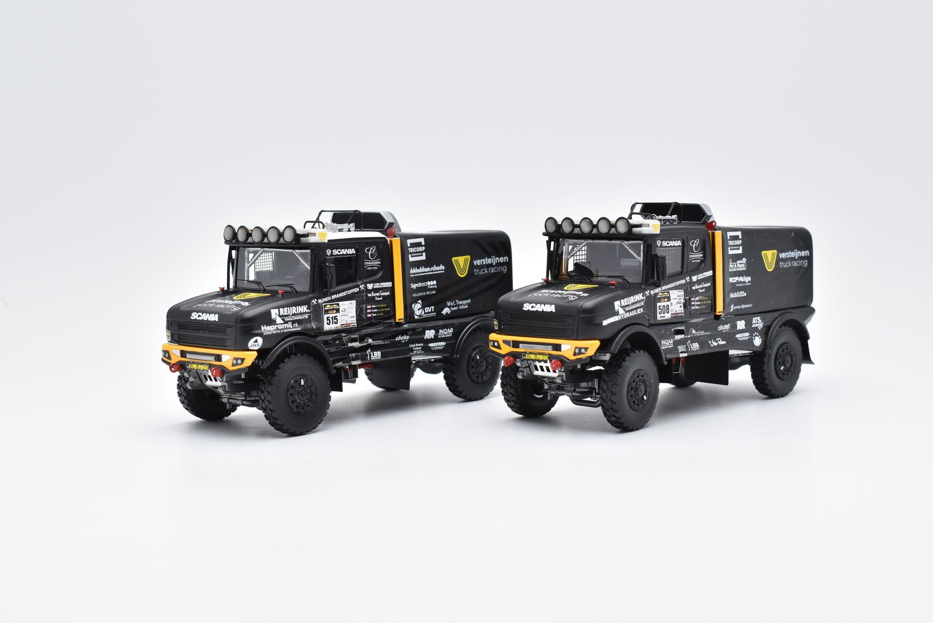 Twee zwarte Unimog-vrachtwagens met gele accenten, versierd met logo's en schijnwerpers.