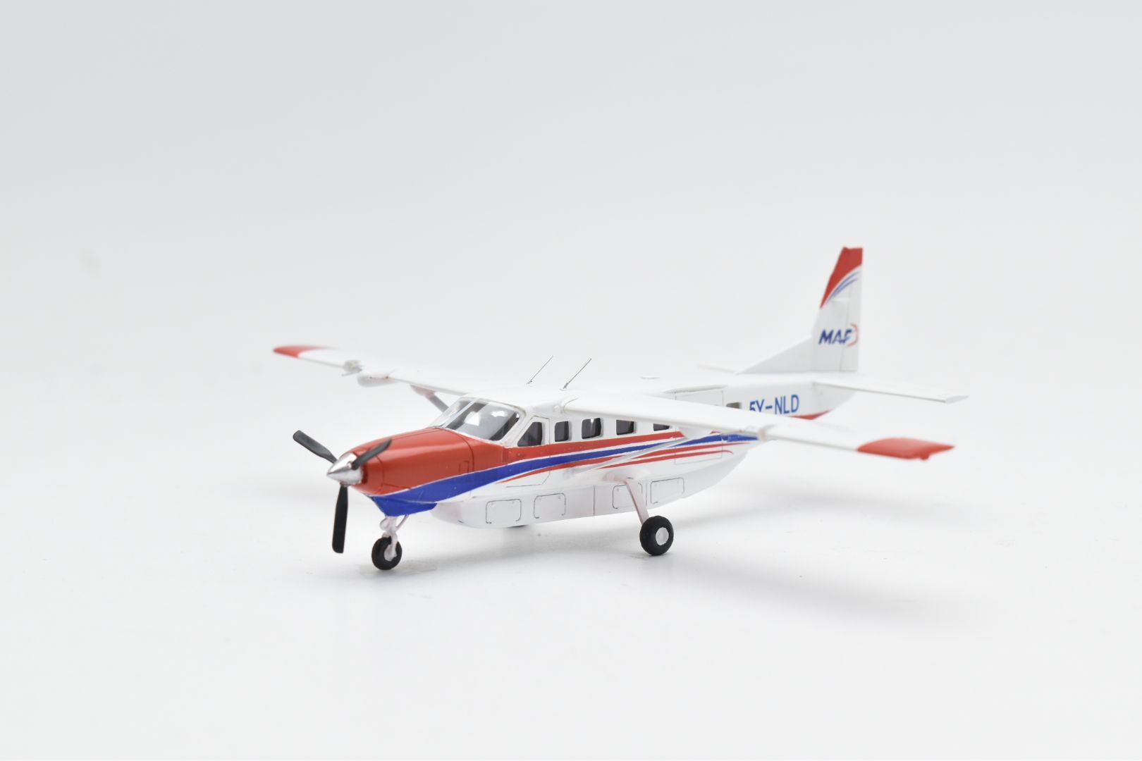 Modelvliegtuig: Cessna 206, rood, wit en blauw, met een propeller, op een witte achtergrond.