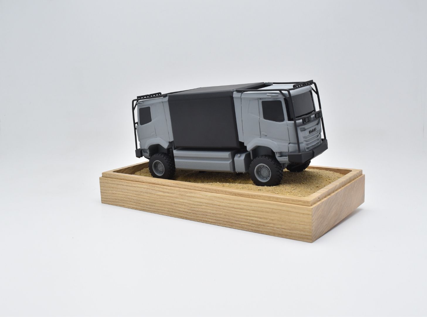 Grijs en zwart speelgoedvrachtwagenmodel op een houten voetstuk.
