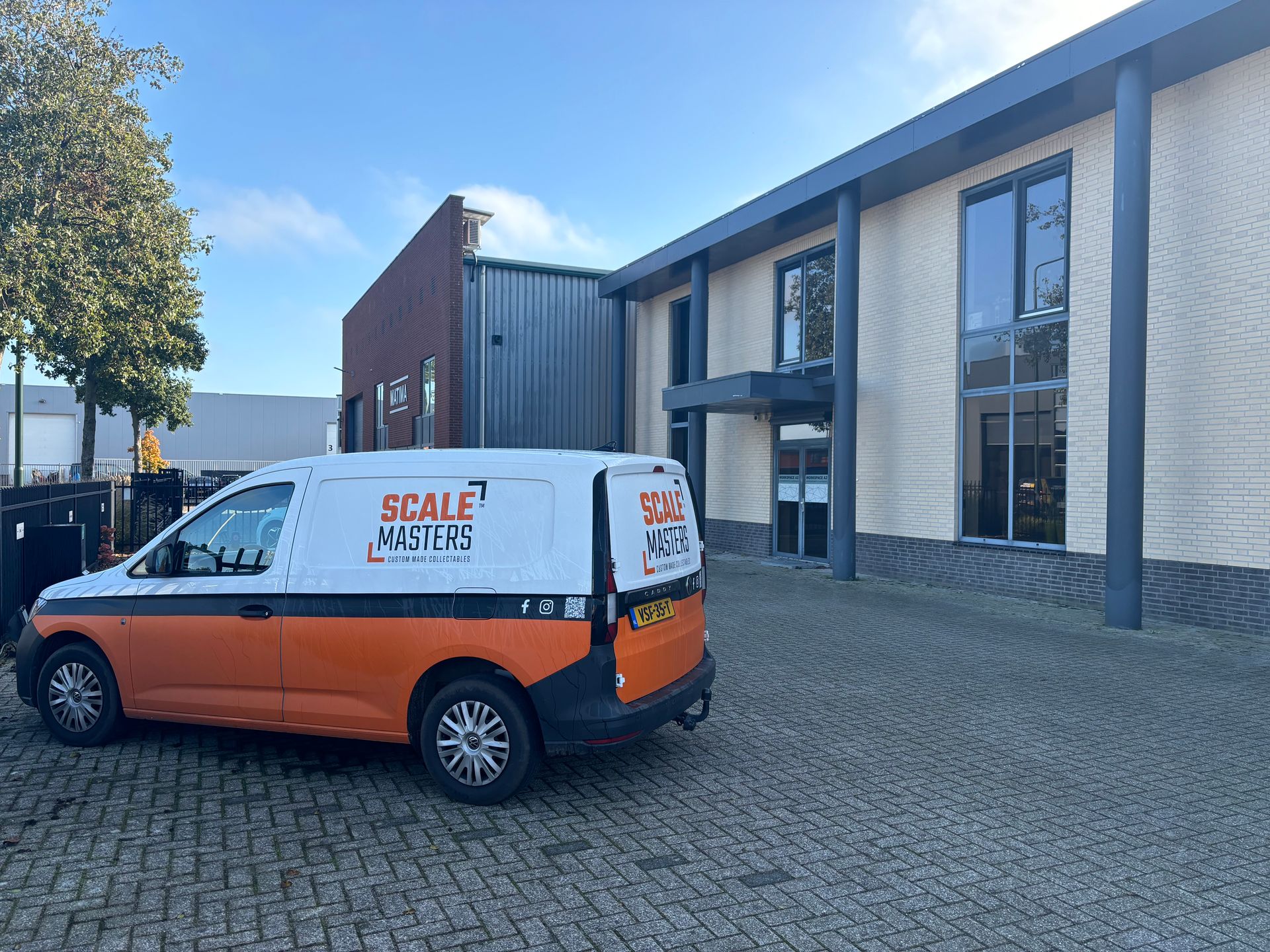Oranje en witte bestelwagen geparkeerd voor een modern gebouw met grijze afwerking en grote ramen.