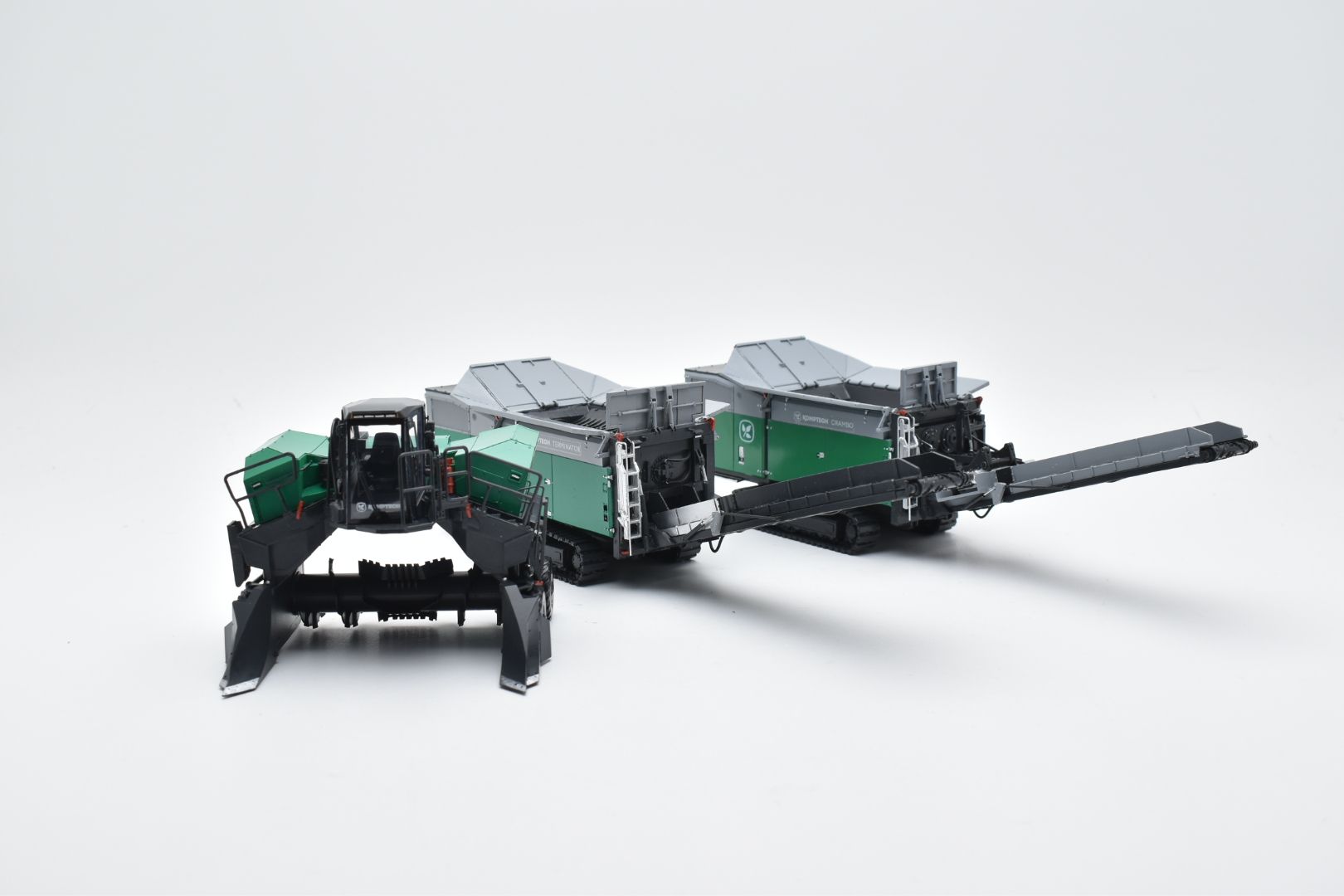 Groene en zwarte industriële machine met twee containers en een lang mes op een witte achtergrond.
