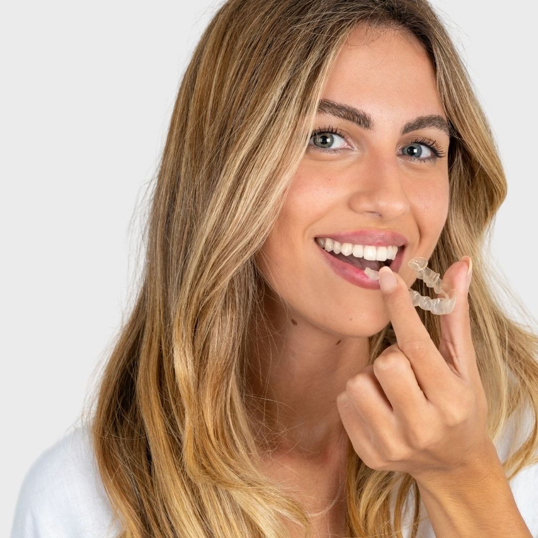 A woman is smiling and holding a clear braces in her mouth