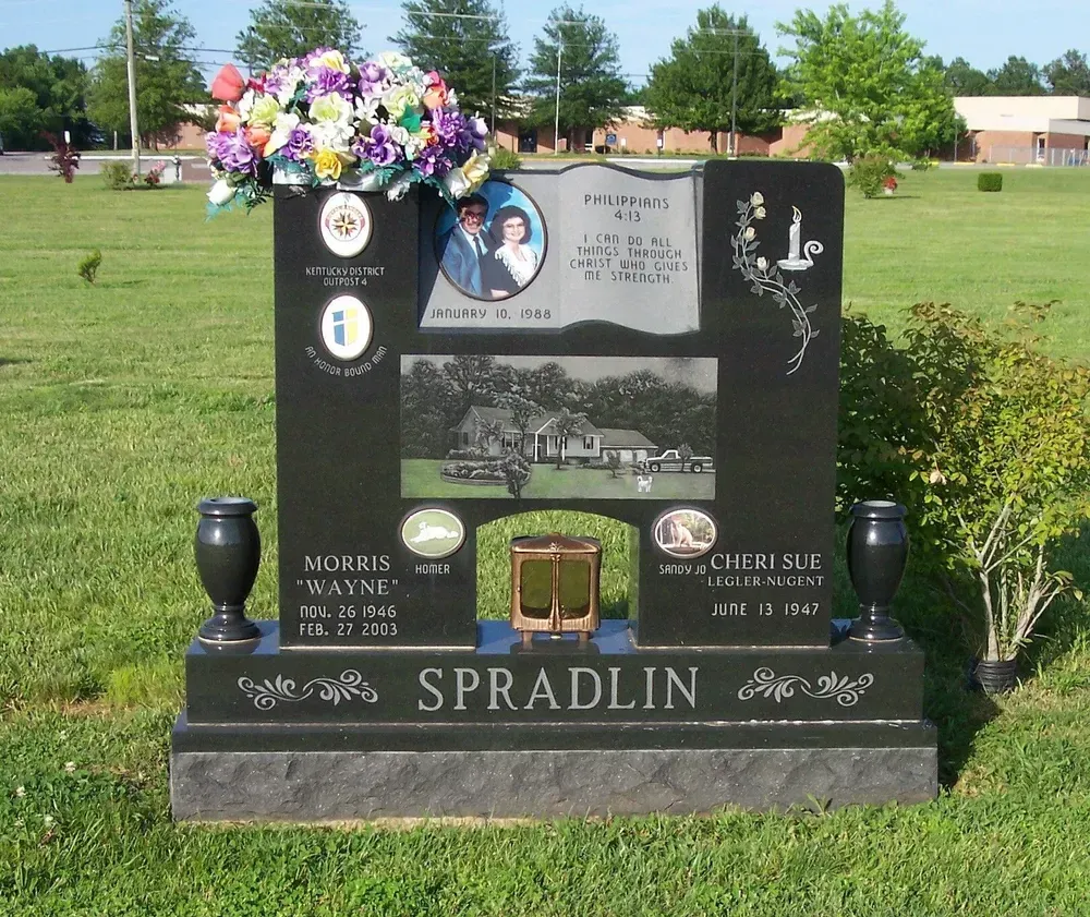 Black granite memorial headstone on a grassy cemetery lawn with colorful flowers on top and the name Spradlin.