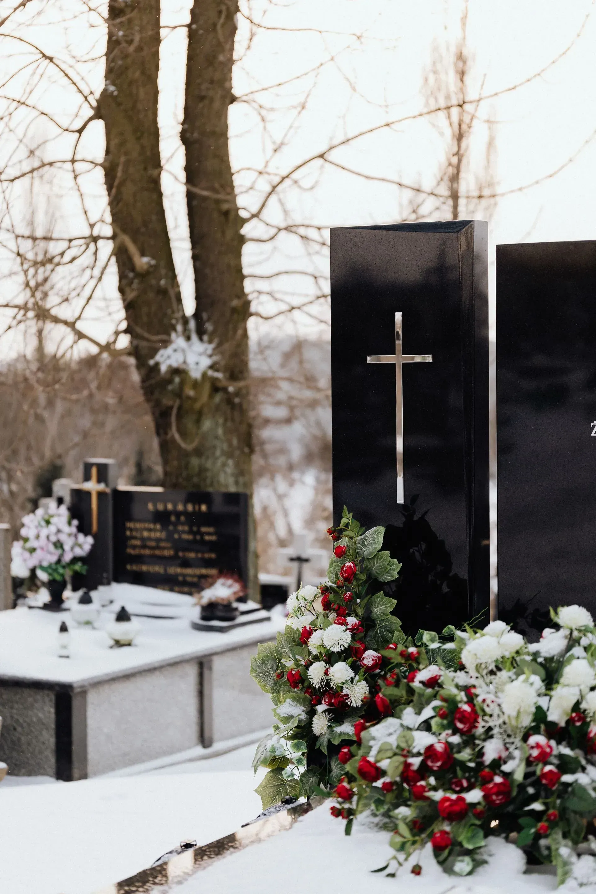 Snow-covered cemetery with black headstones and white-red floral wreaths