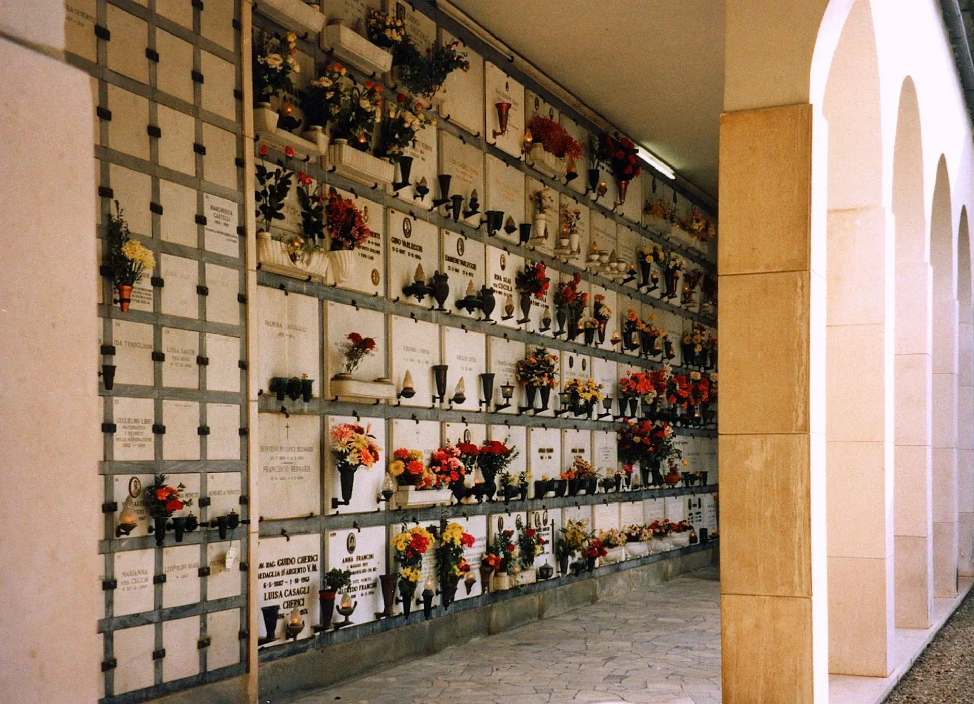 Columbarium wall with rows of flower-adorned memorial niches in a covered corridor
