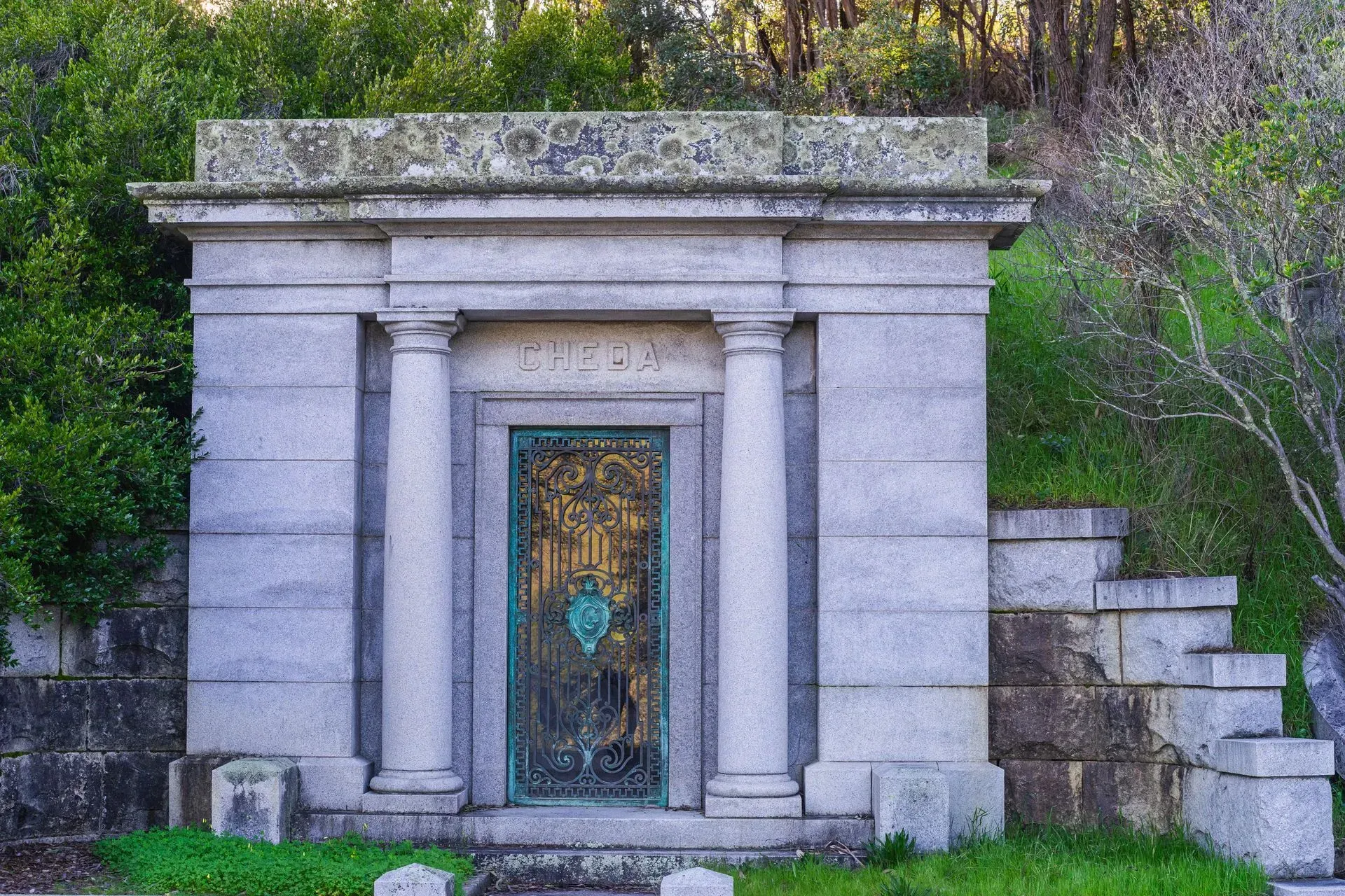 Stone mausoleum with ornate metal door set into a hillside cemetery