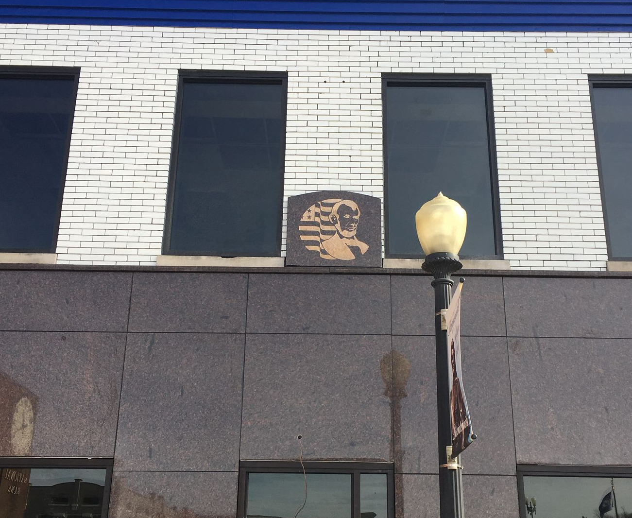 Brick building facade with tall windows, a small sign, and a streetlamp in front