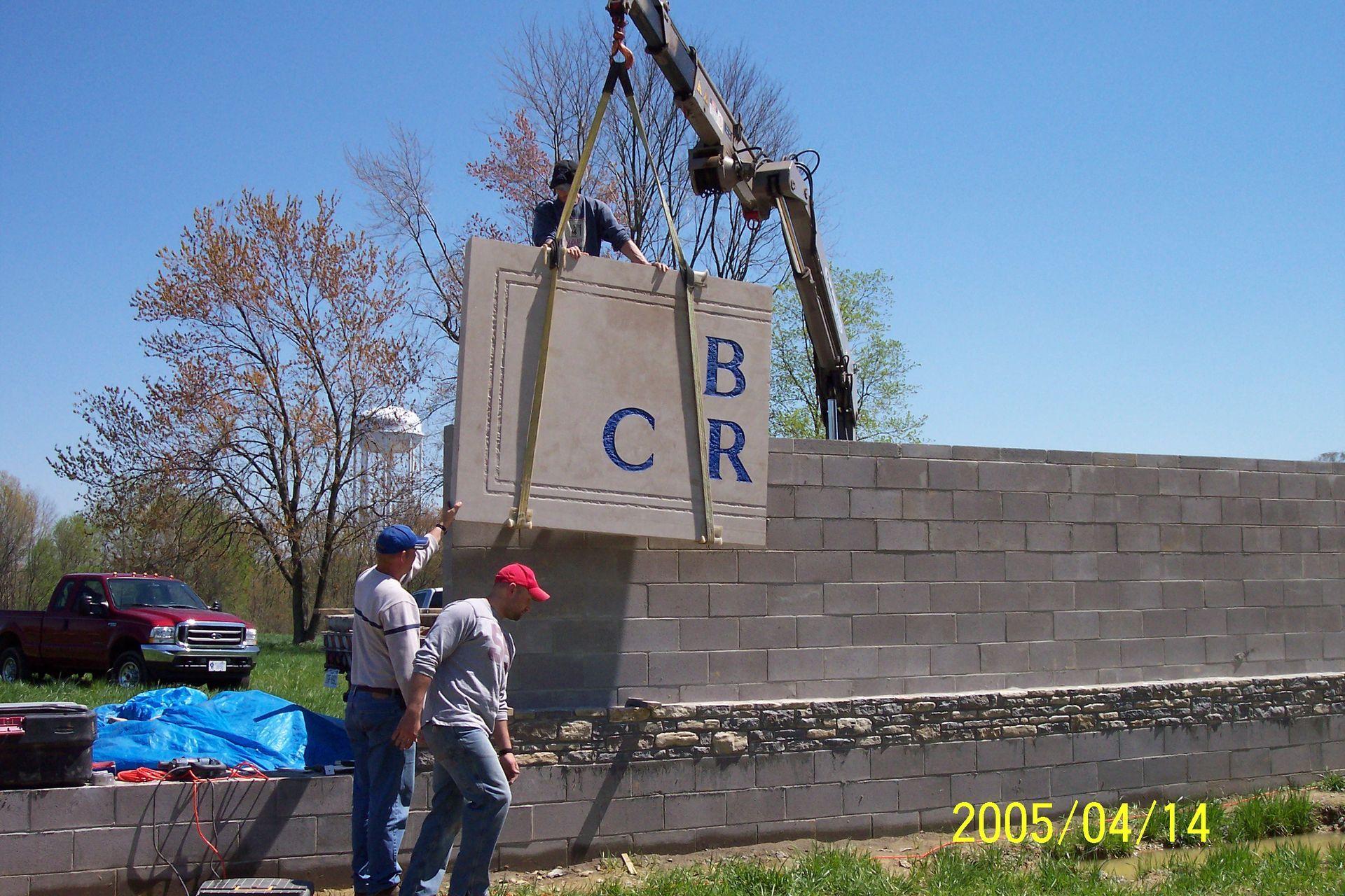Workers moving a large concrete slab beside a block wall at a construction site