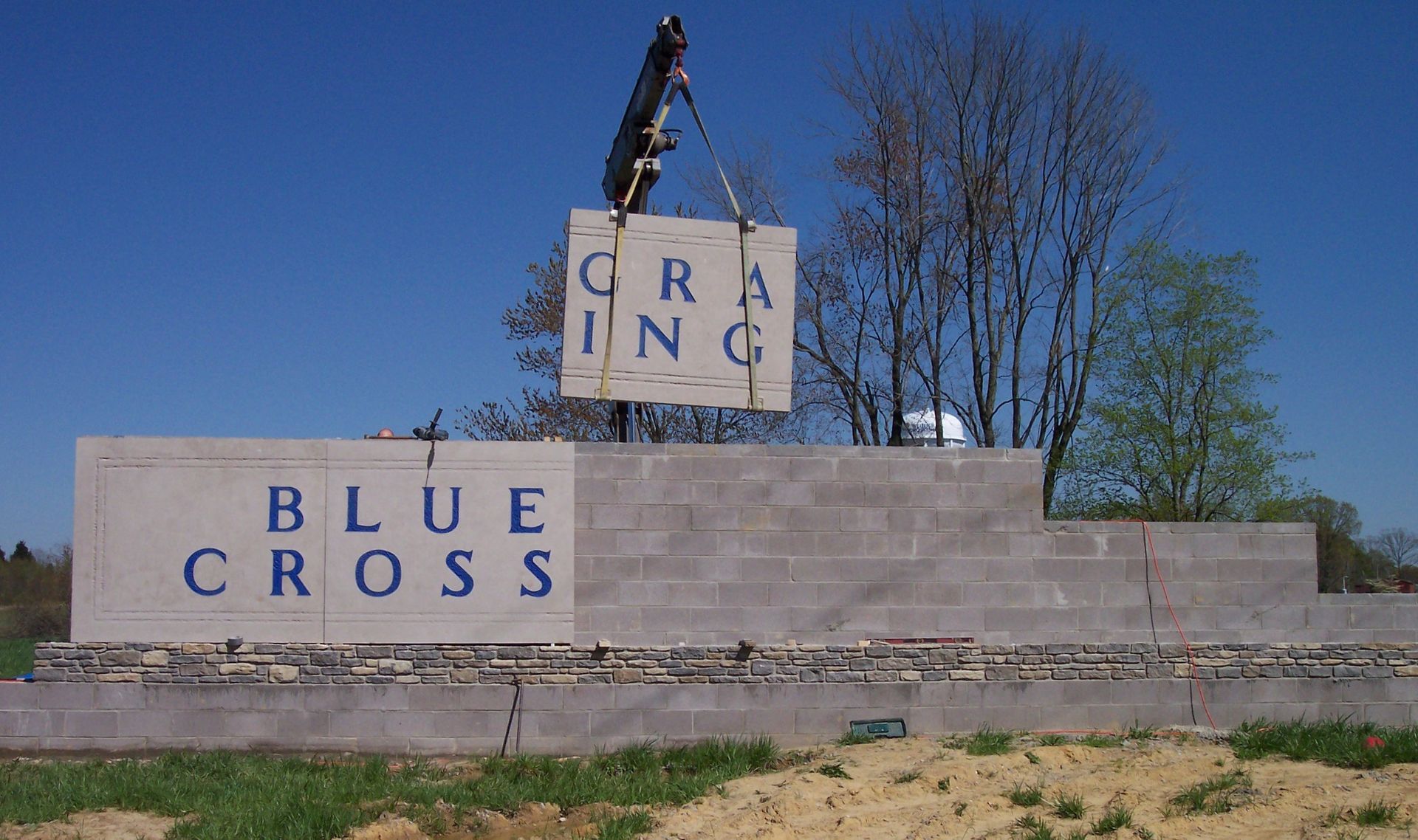 Blue Cross sign on a stone base with a small sculpture above it outdoors