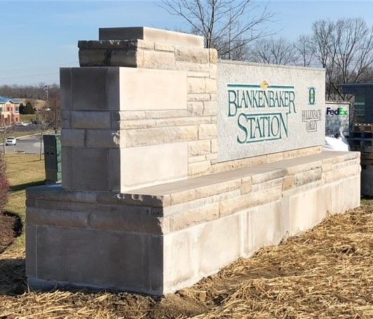 Stone entrance sign for Baw-Beese Station on a grassy roadside.