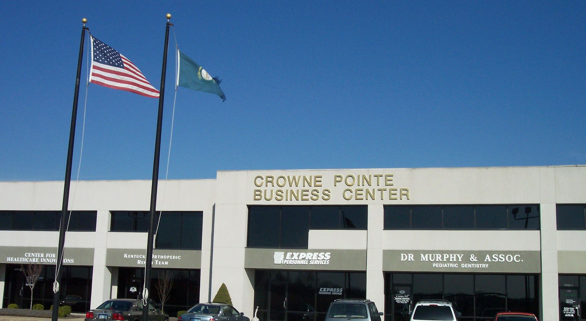 Crowne Pointe Business Center storefront with American and state flags against a clear blue sky