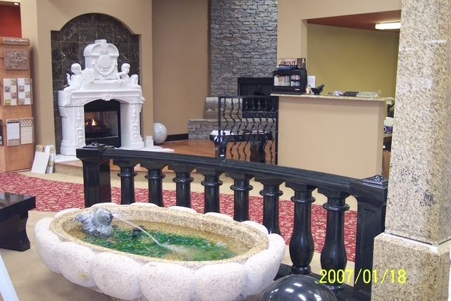 Indoor lobby with decorative fountain, black railing, and ornate white fireplace on a stone wall