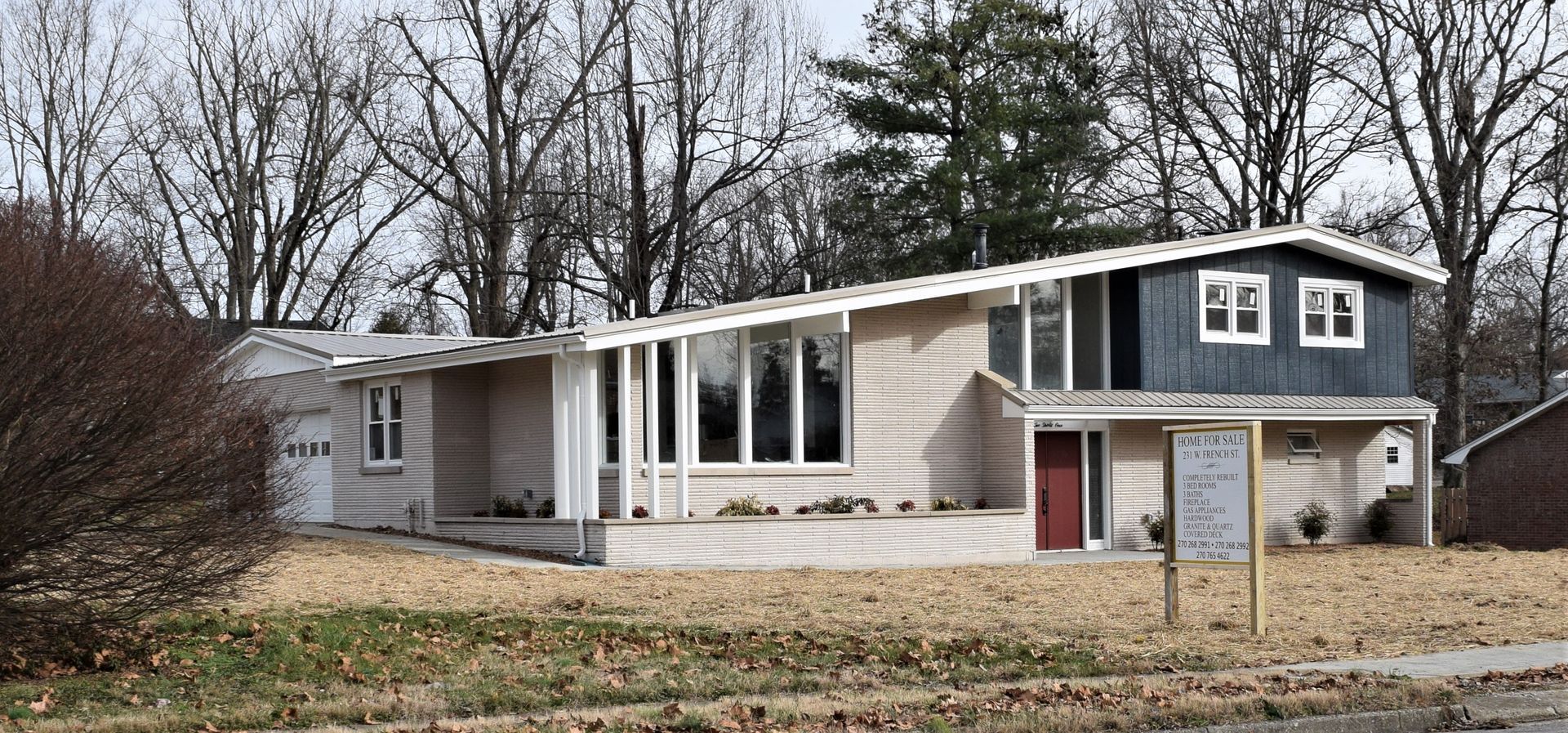 Small modern house with damaged white exterior and a sign in front on a cloudy day