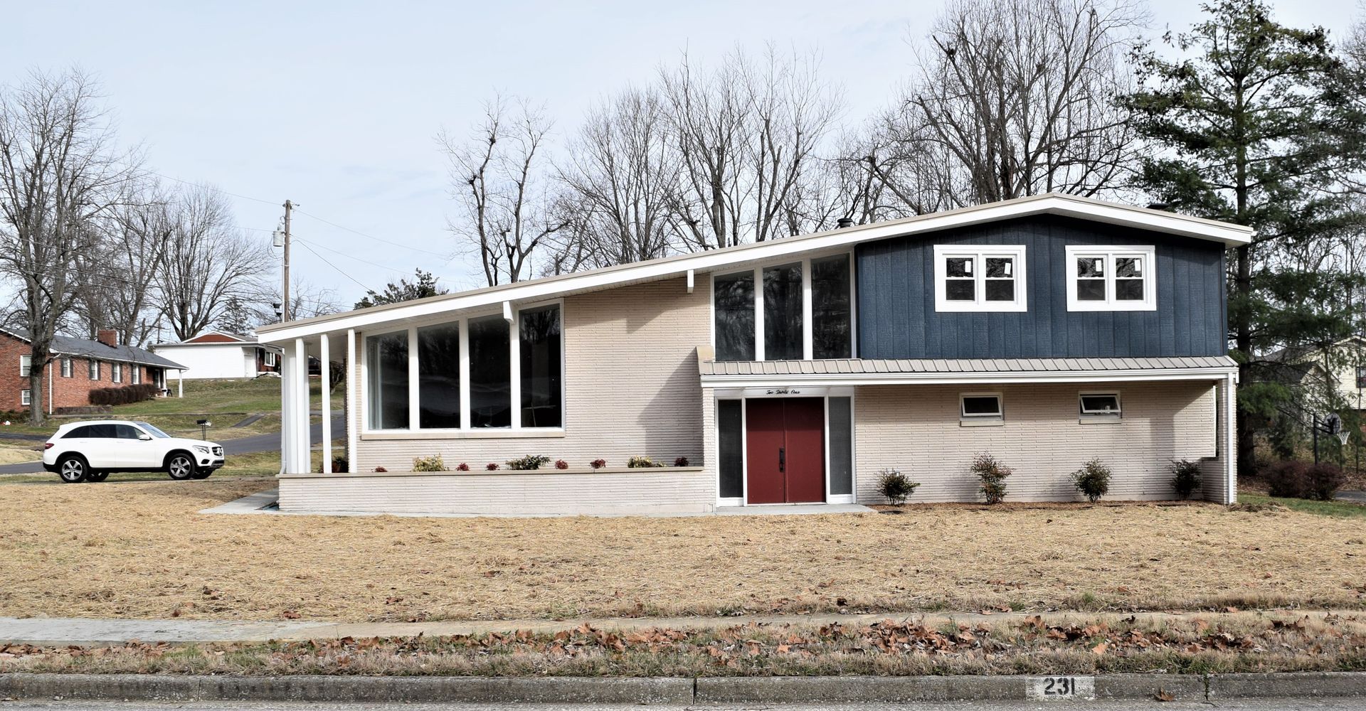Suburban split-level house with gray siding, white trim, red doors, and a car parked on the lawn