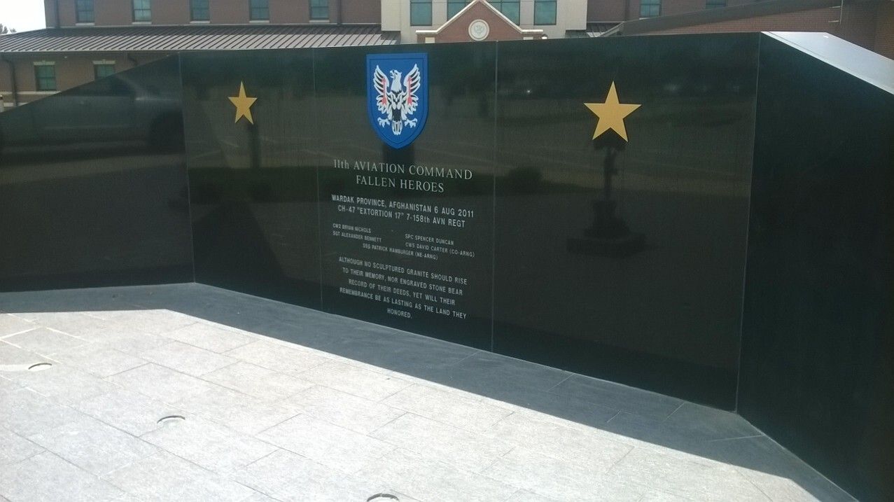 Black memorial wall with gold stars and engraved text in a sunlit outdoor plaza
