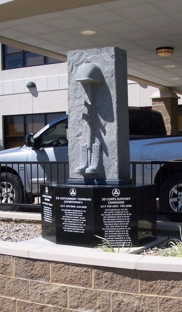 Stone memorial monument with raised figure and black name plaques outside a building