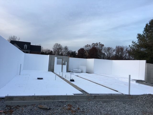 Snow-covered construction site with white foundation walls under a cloudy sky.