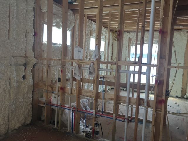 Unfinished room under construction with exposed studs, insulation, and window openings exposed to daylight