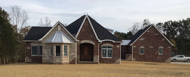 Large brick house with multiple gables, front porch, and attached garage on a grassy lot
