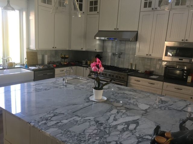 Modern kitchen with a large marble island and a vase of pink flowers on the counter.