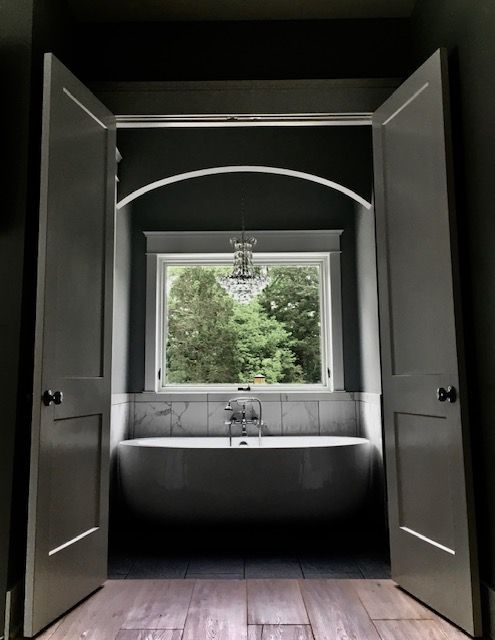 Open bathroom doors framing a clawfoot tub beneath a window with garden view.