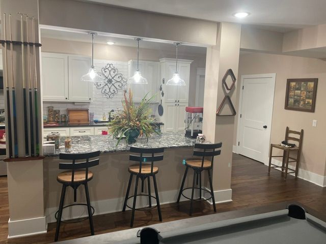 Modern kitchen with granite island, three bar stools, white cabinets, and hardwood floors.