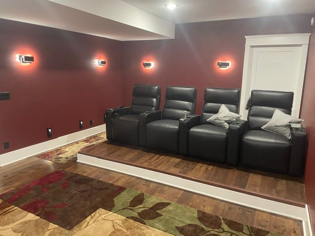 Home theater room with four black recliners, red walls, wall sconces, and a patterned rug