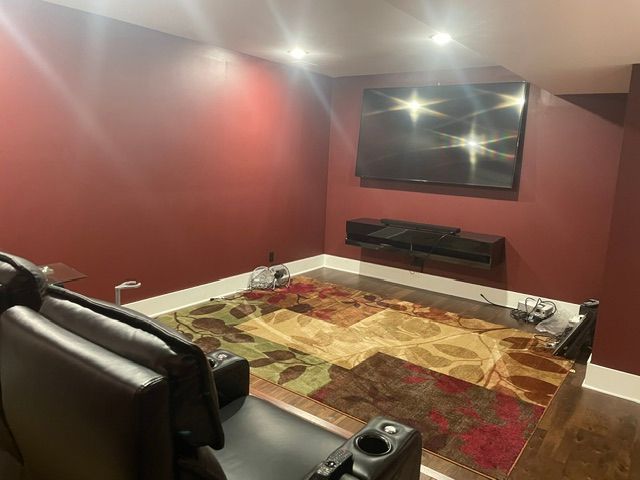 Empty living room with burgundy walls, patterned rug, wall-mounted TV, and black leather chair with ottoman.
