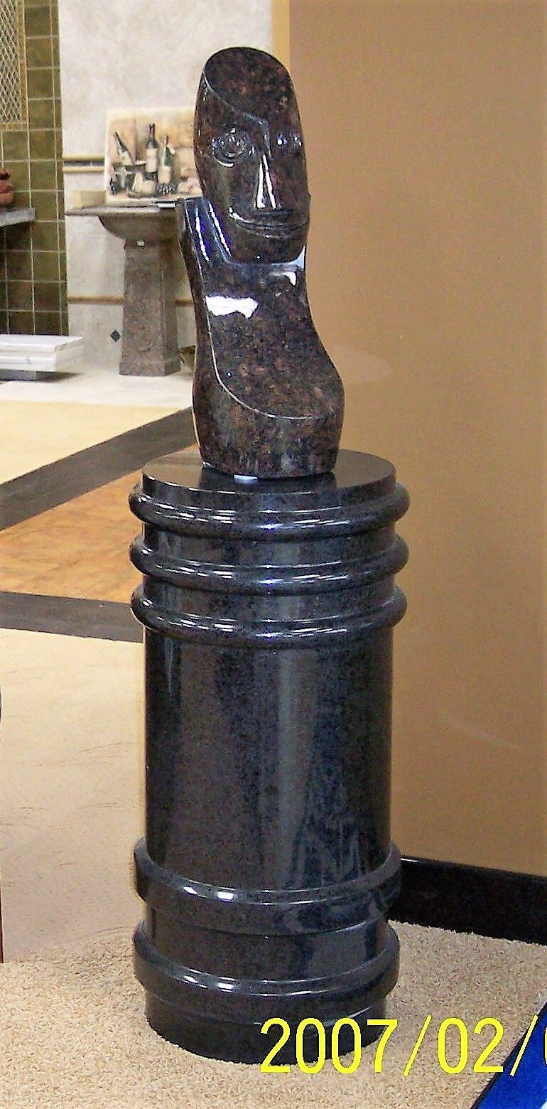 Black carved wooden statue on a dark pedestal in an indoor lobby.